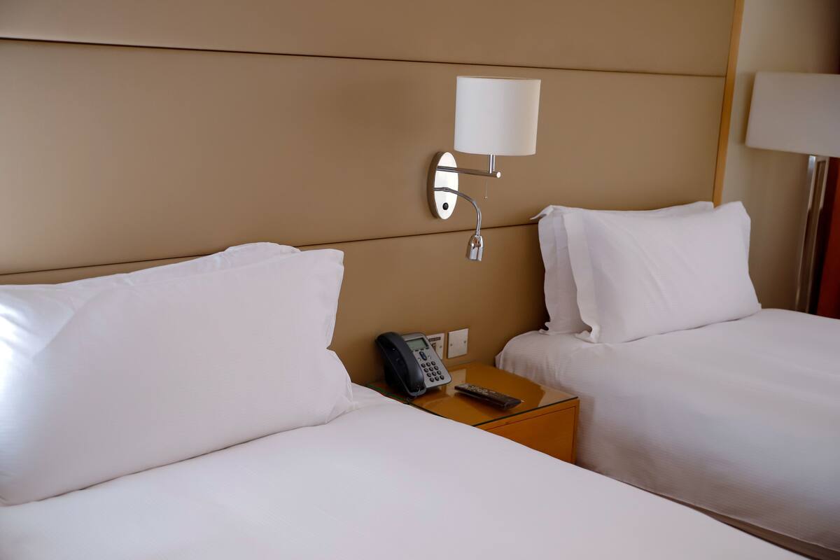 Habitación de hotel con dos camas, una mesita de noche con teléfono y una lámpara de pared.