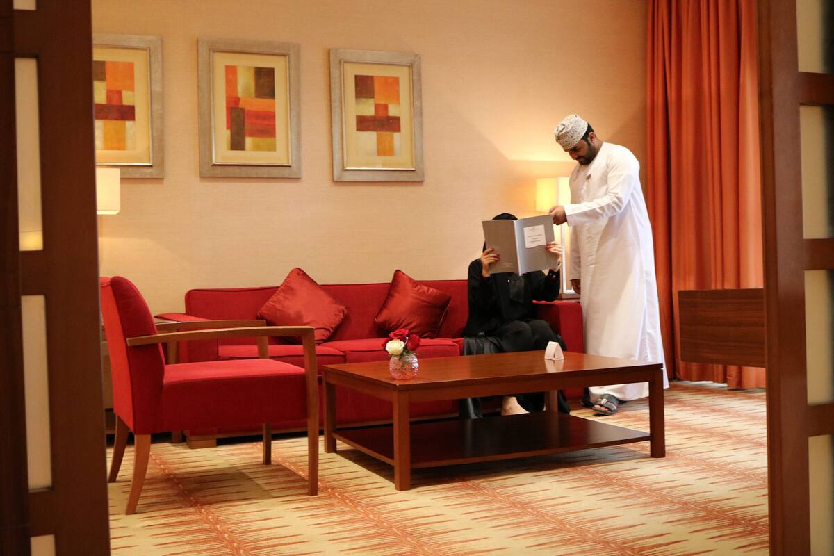 Una habitación de hotel con un sofá rojo, una mesa de centro de madera y una persona leyendo un libro.