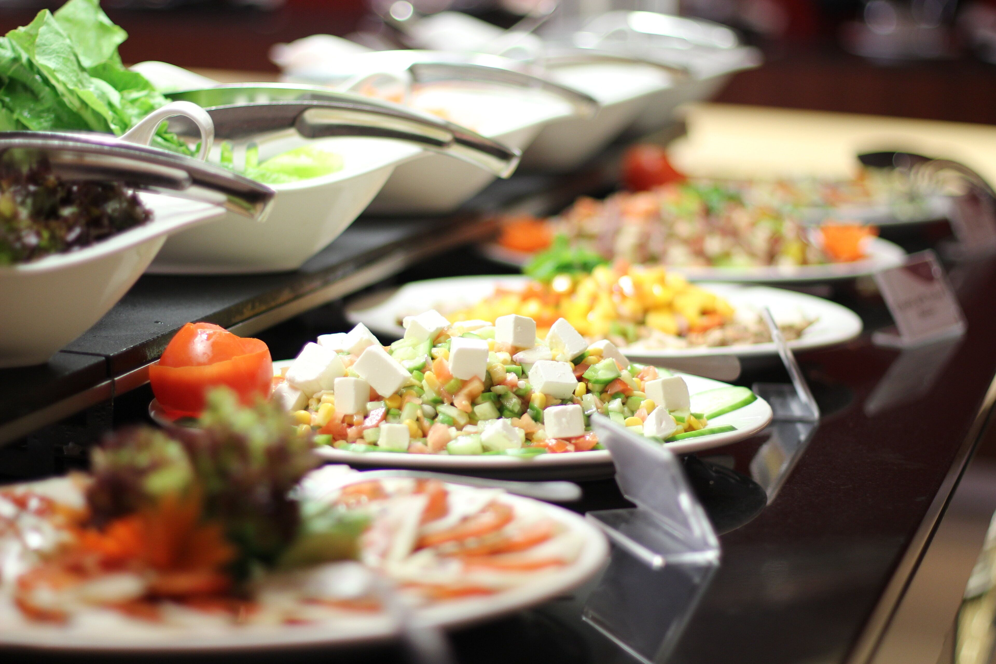 A buffet with various dishes including salads, vegetables, and cheese.