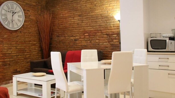 A modern living space with a brick wall, a white dining area, and a kitchen with a microwave. - Travessera Parc Guell Apartamentos (Barcelona)