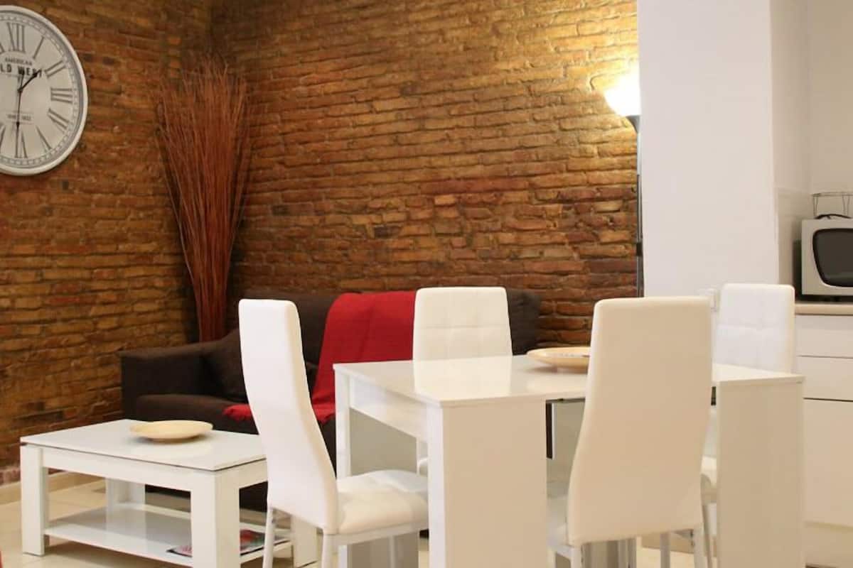 A modern living space with a brick wall, a white dining area, and a kitchen with a microwave.