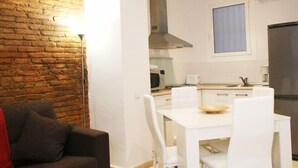 A compact kitchen with white cabinetry, a stainless steel refrigerator, and a dining area with a white table and chairs. - Travessera Parc Guell Apartamentos (Barcelona)
