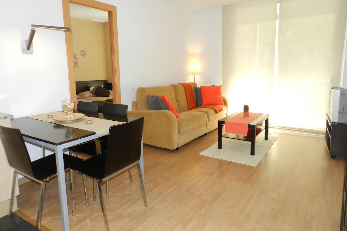 A modern living room with a sofa, coffee table, dining table, chairs, and a TV.