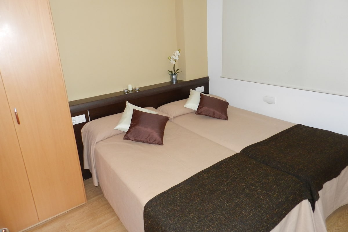 A hotel room with a bed, two pillows, a bedside table with a vase of flowers, and a wooden wardrobe.