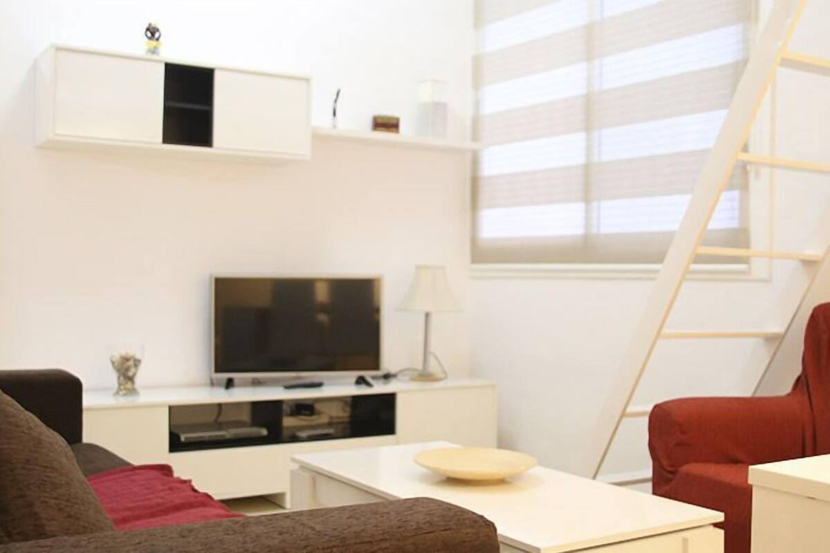 A living room with a TV, a white cabinet, a red chair, and a ladder against a window.