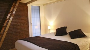 A bedroom with a bed, a nightstand, a lamp, and a window with blinds. - Travessera Parc Guell Apartamentos (Barcelona)