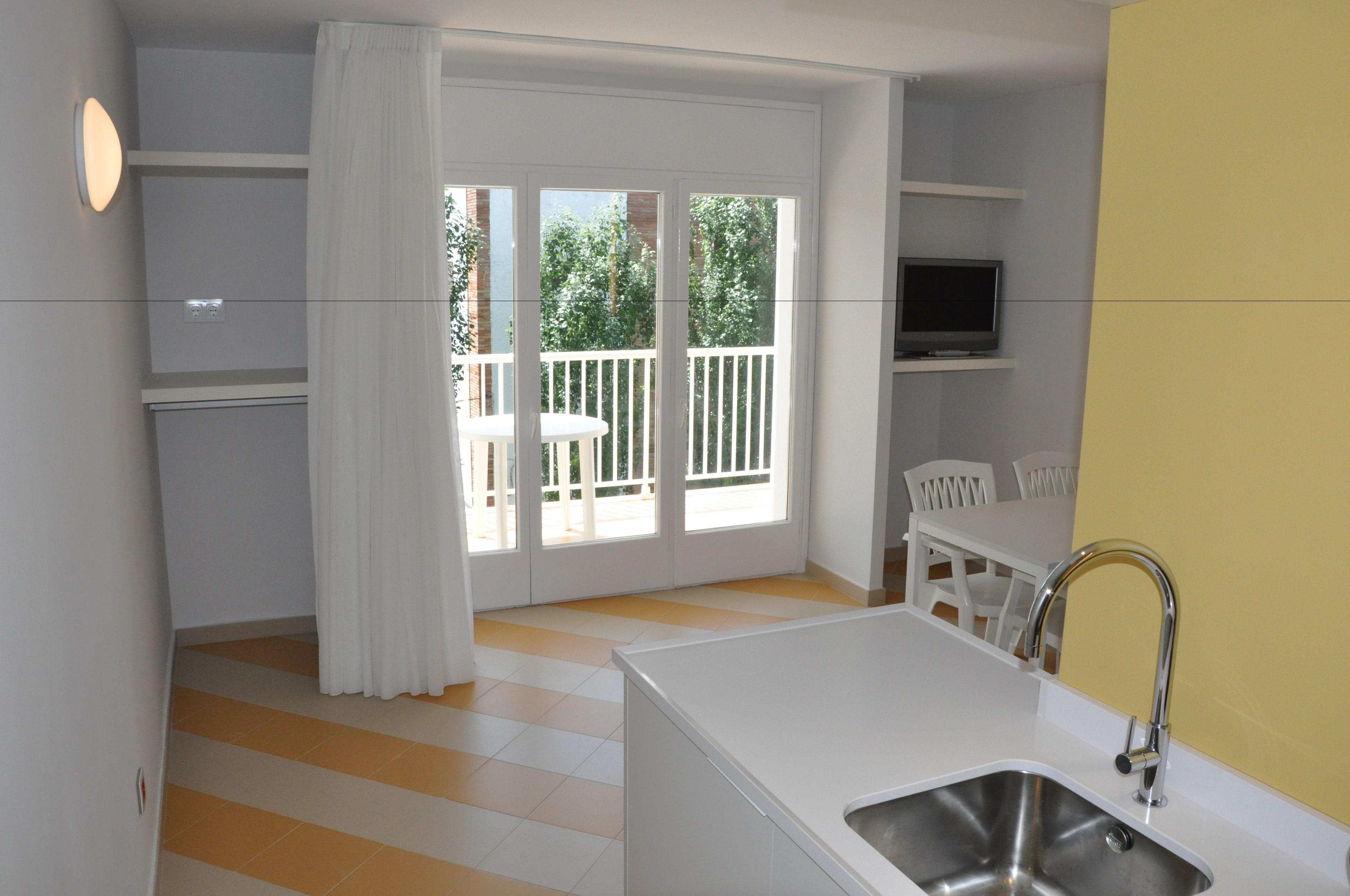 A compact kitchen with a sink, a dining table, and a TV mounted on the wall.