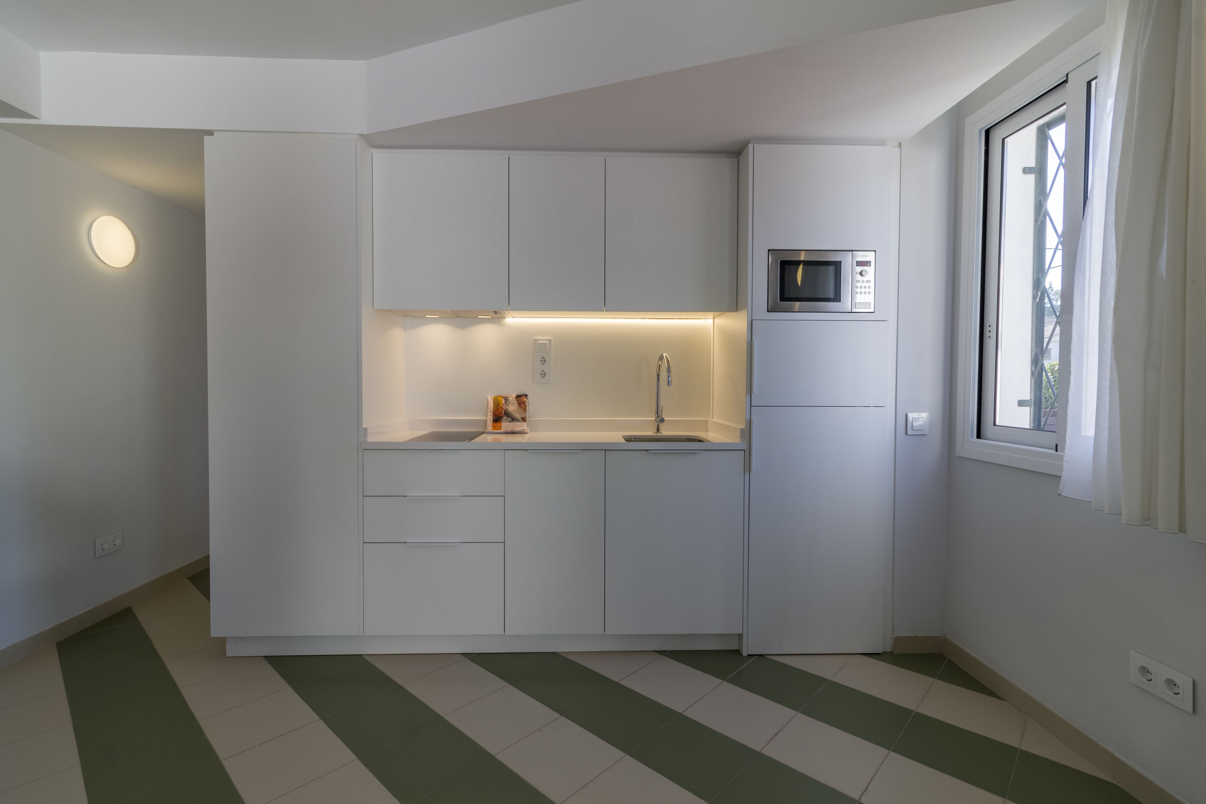 Una cocina compacta con armarios blancos, un microondas integrado y un lavamanos pequeño.