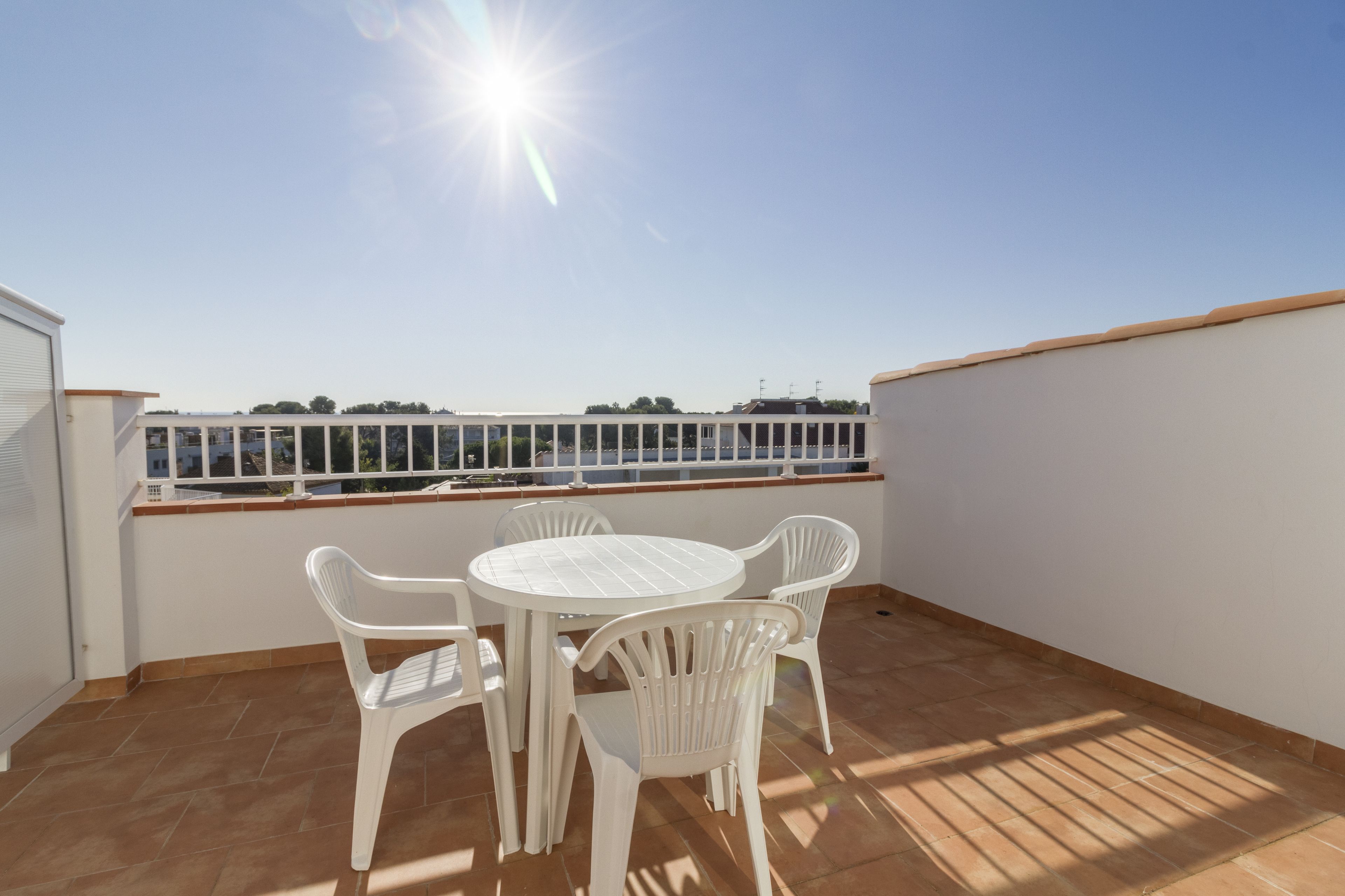 Una terraza en la azotea con una mesa y sillas blancas, vistas al mar y un cielo despejado.
