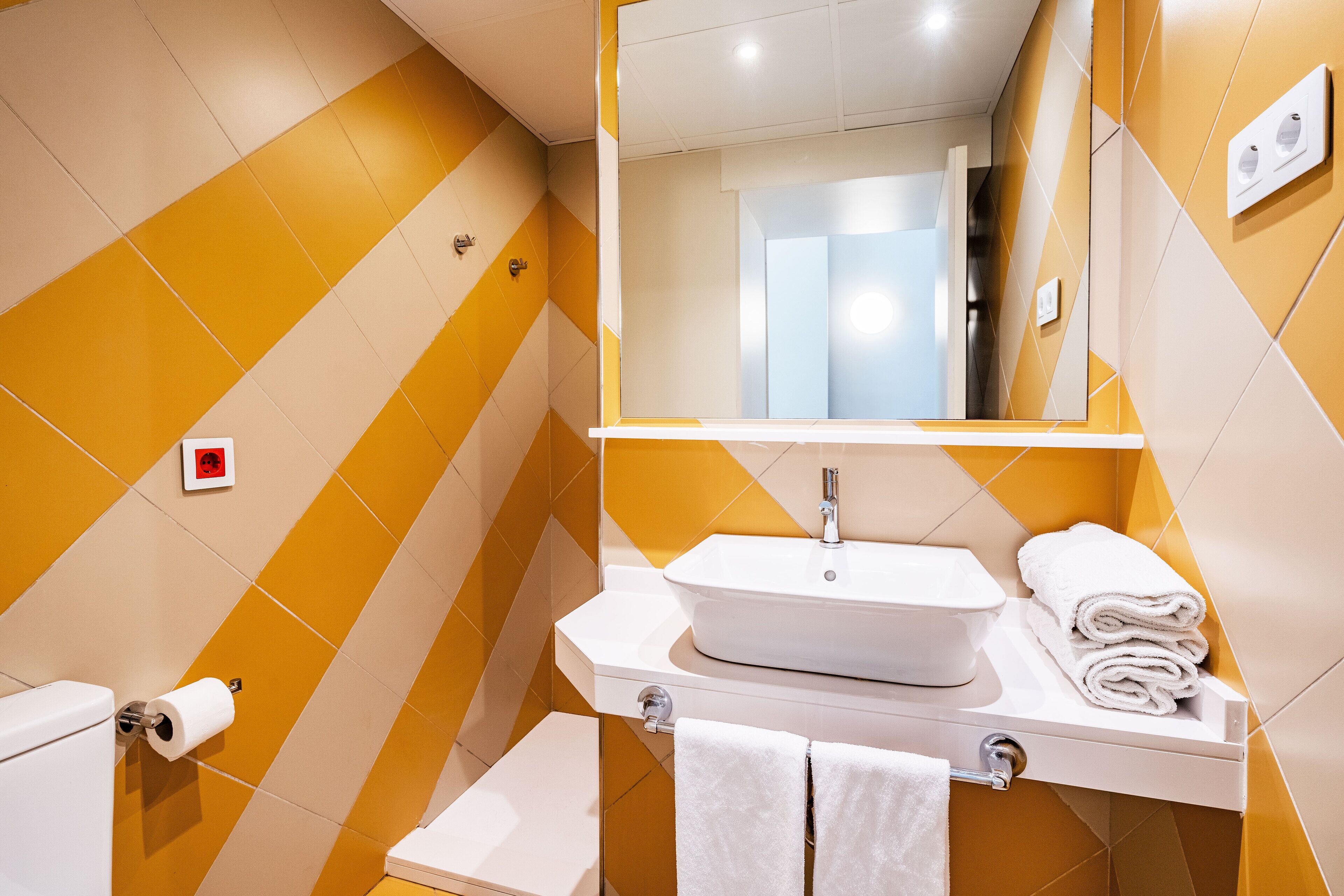Un baño con lavamanos, espejo e inodoro blancos.