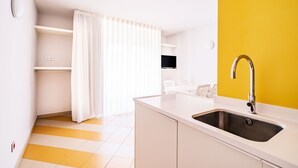 Una cocina con encimera blanca, pileta de acero inoxidable y una pared de acento amarilla.