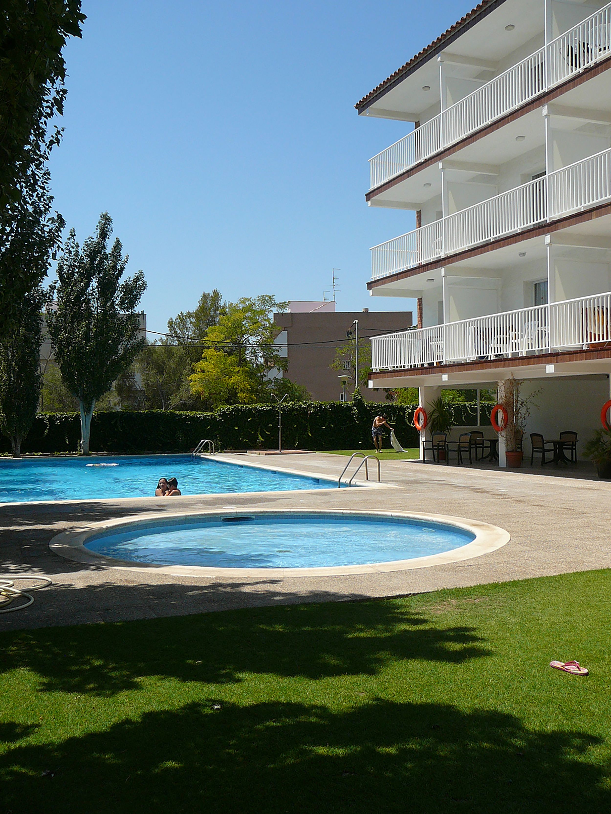 Una piscina con un área verde circundante y un edificio de varios pisos con balcones.