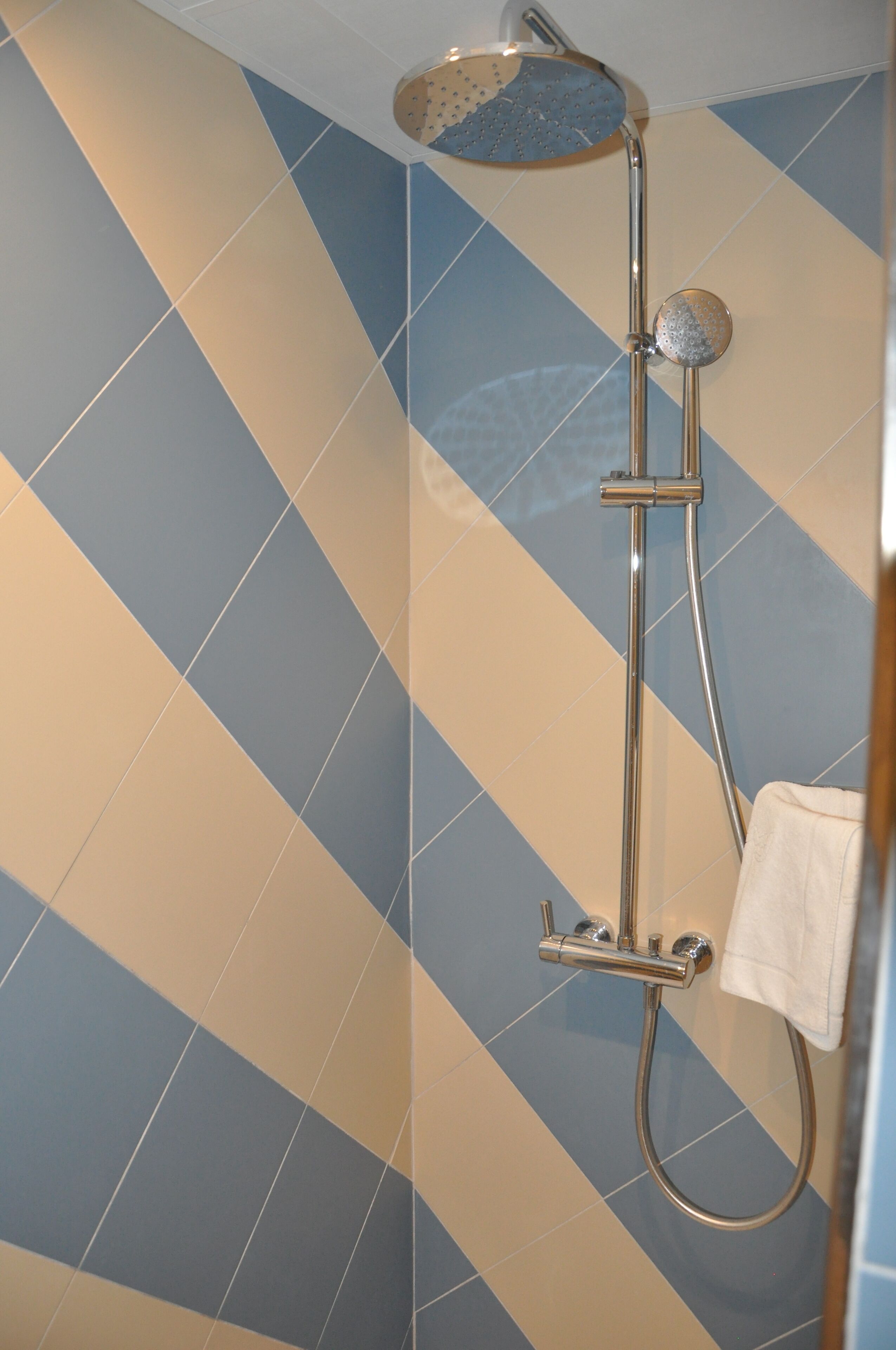 Ducha con cabezal de ducha de mano y grifo empotrado en una pared con azulejos azules y beige.