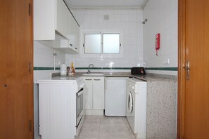 A compact kitchen with white cabinetry, a built-in oven, a washing machine, and a double sink. - Apartments Sunway Tara (Sitges)