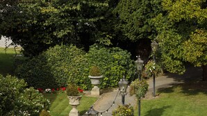A garden pathway with stone planters and hanging flower baskets, surrounded by lush greenery and trees. - The Victoria Hotel (Canterbury)