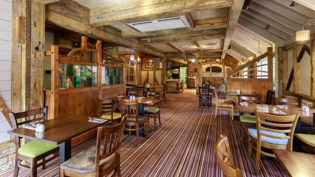 A rustic interior with wooden beams, a striped floor, and a variety of seating arrangements including tables and benches. - The Victoria Hotel (Canterbury)