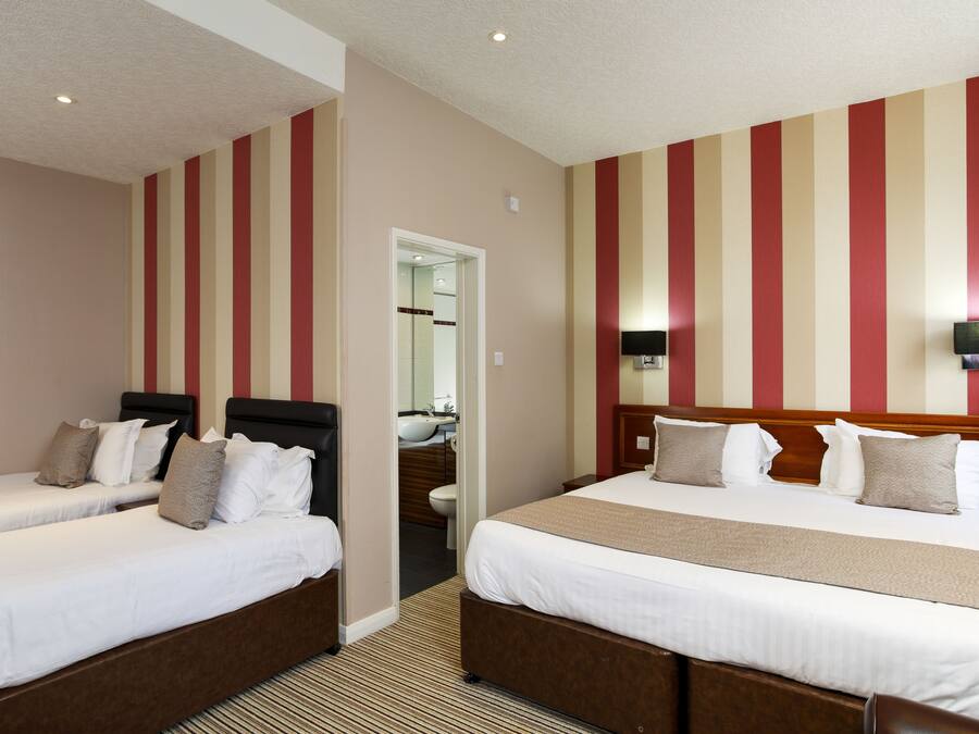 A hotel room with two single beds, a large bed, a bathroom with a mirror, and a TV mounted on the wall.
