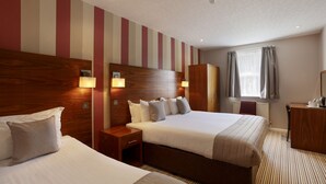 A hotel room with two beds, wooden headboards, bedside lamps, a desk, and a window with curtains. - The Victoria Hotel (Canterbury)