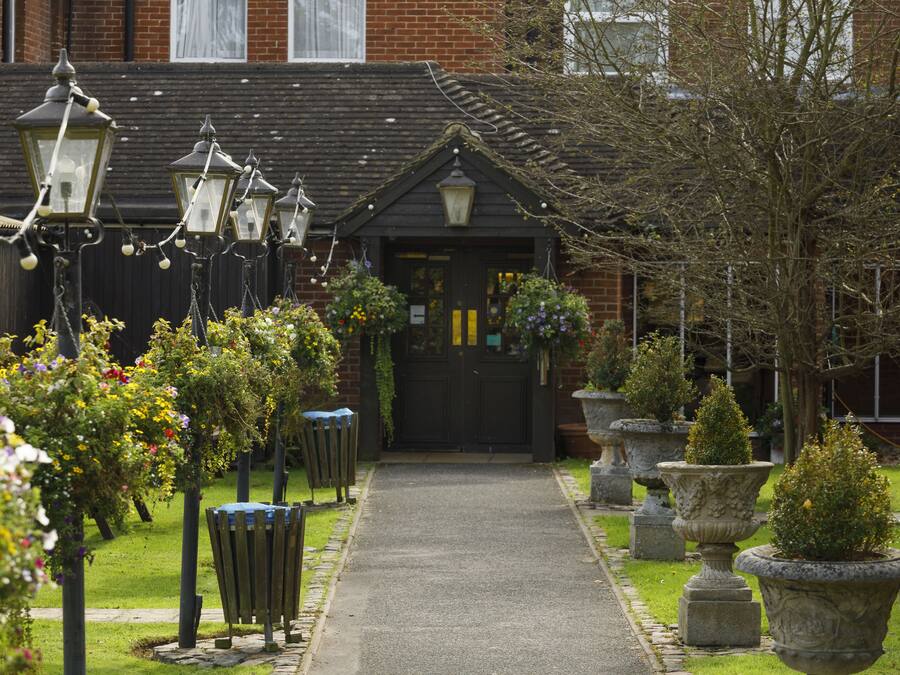 A pathway leading to a building with a dark entrance, surrounded by flower beds and stone planters.