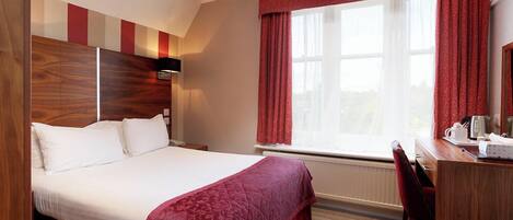 A hotel room with a large bed, a desk, and a window with curtains.