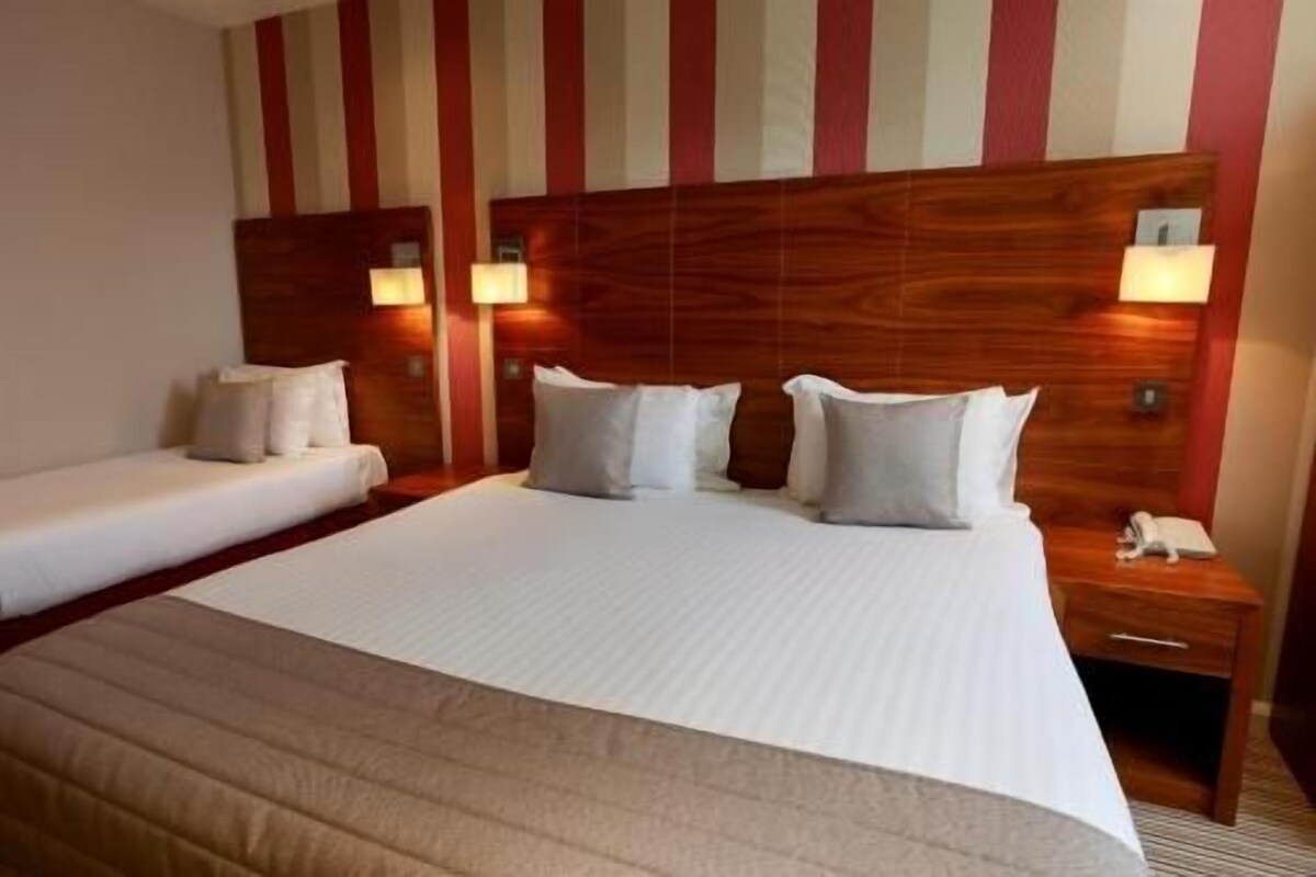 Ein Hotelzimmer mit einem großen Bett, zwei Nachttischen, einer Wandlampe und einem kleinen Tisch.