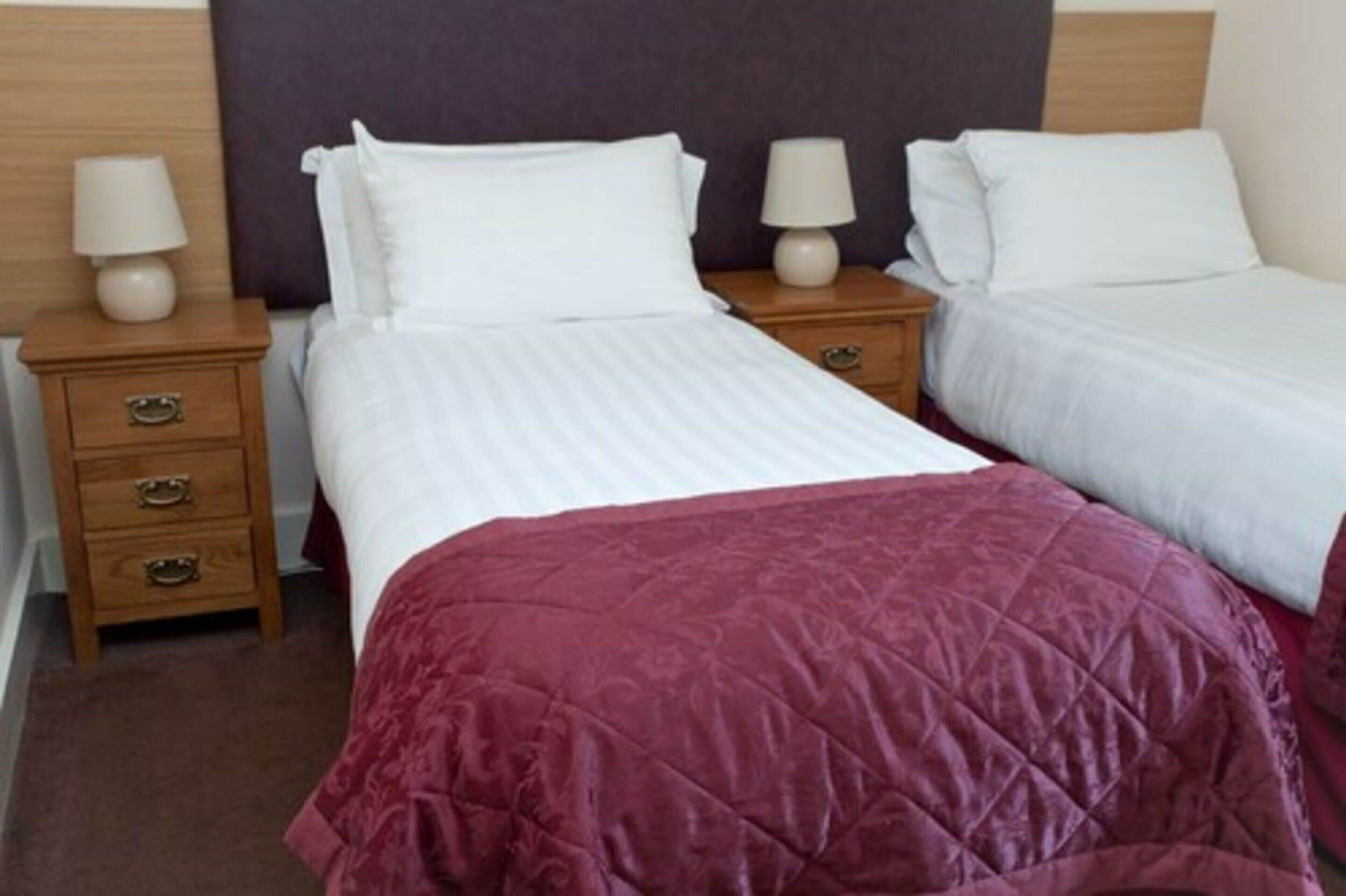 A hotel room with two single beds, each with white linens and a wooden nightstand with a lamp.