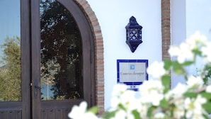 Entrada de un hotel con una puerta de madera, un letrero azul que dice "Caserio de Iznajar" y un farol decorativo.