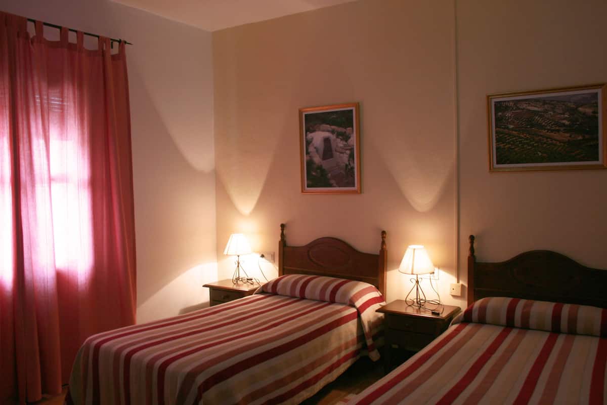 Una habitación de hotel con dos camas, cada una con ropa de cama a rayas, cabeceros de madera y lámparas de noche.
