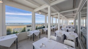A restaurant with white tables and chairs, large windows, and a view of the beach. - Nautilus Family Hotel (Pesaro)