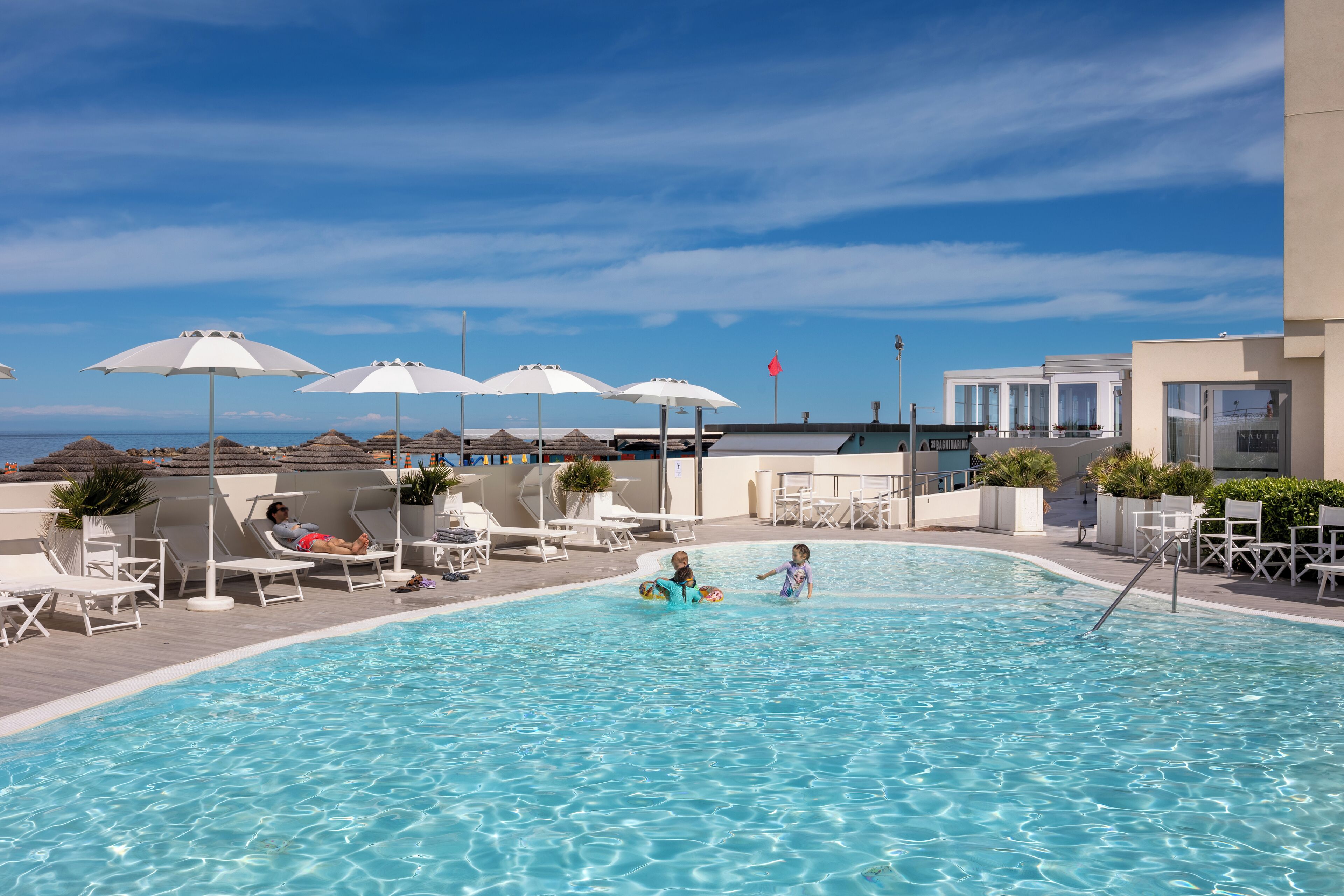 Piscina com espreguiçadeiras e guarda-sóis, rodeada por edifícios e um céu claro.