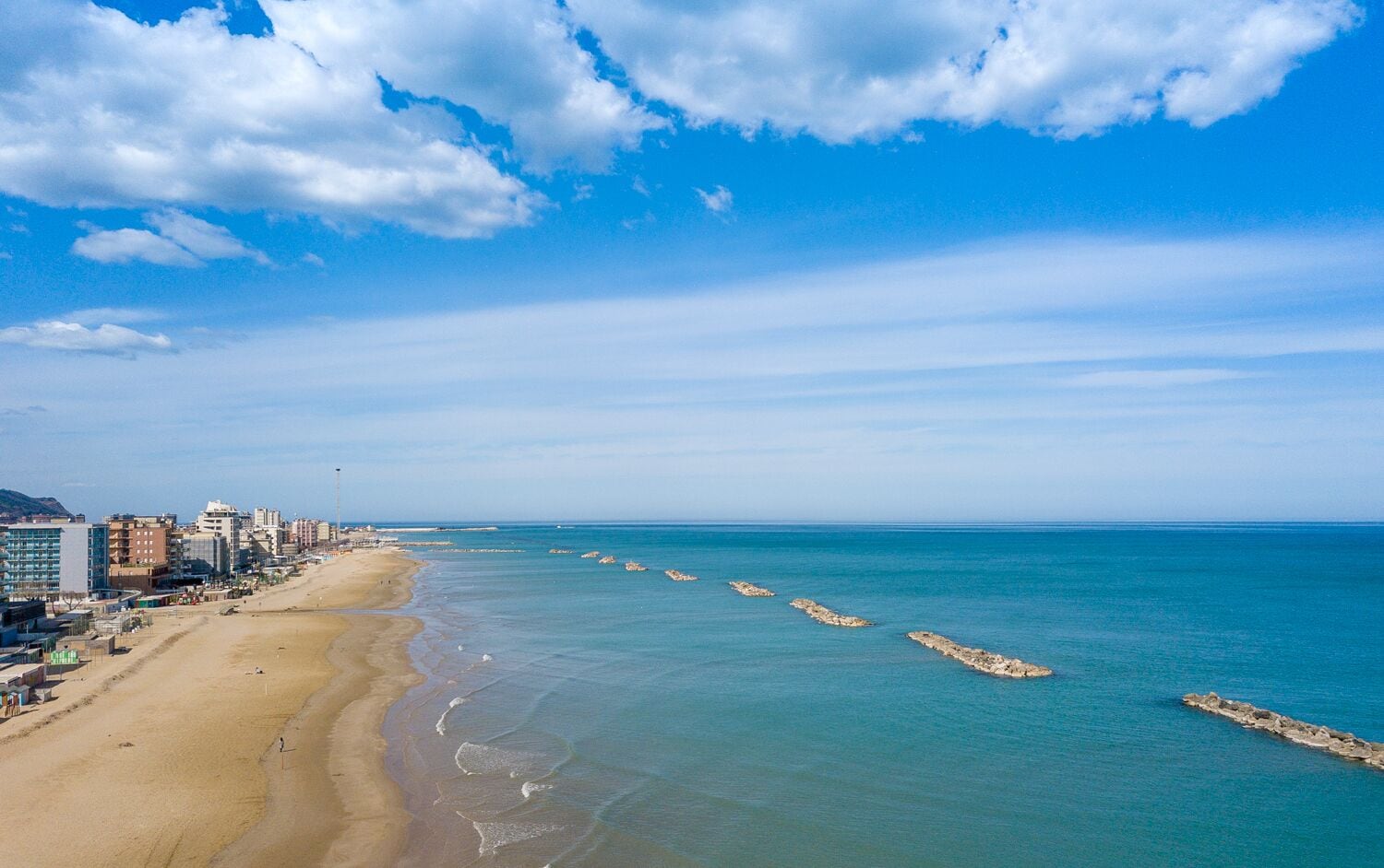Un paysage urbain côtier avec une vaste plage de sable, une mer bleue et limpide, et des bâtiments qui bordent la côte.