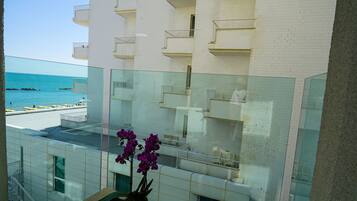 Un balcón con vista a la playa, una orquídea en maceta y una mesa blanca.