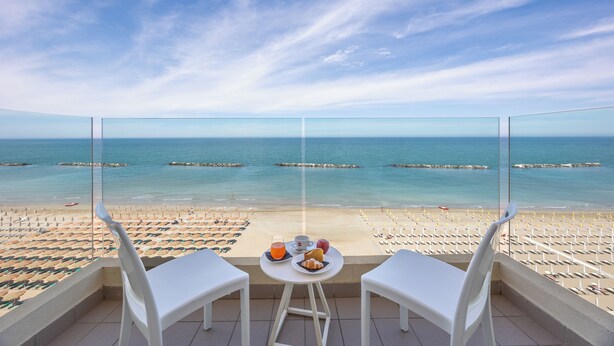 A balcony with a table set for two, overlooking a beach with umbrellas and lounge chairs. - Nautilus Family Hotel (Pesaro)