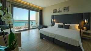 A modern hotel room with a large bed, a balcony with a view of the beach, and a potted orchid on the left. - Nautilus Family Hotel (Pesaro)