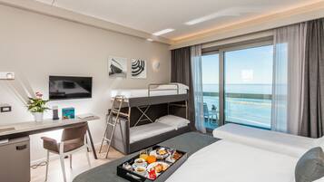 Une chambre d’hôtel moderne équipée d’un lit superposé, d’un bureau avec une chaise, d’une télévision et d’un balcon offrant une vue sur la mer.