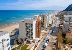 A coastal hotel with a swimming pool, a beach view, and a parking area.