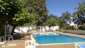 Piscina con borde de baldosas, rodeada de árboles y mobiliario exterior.