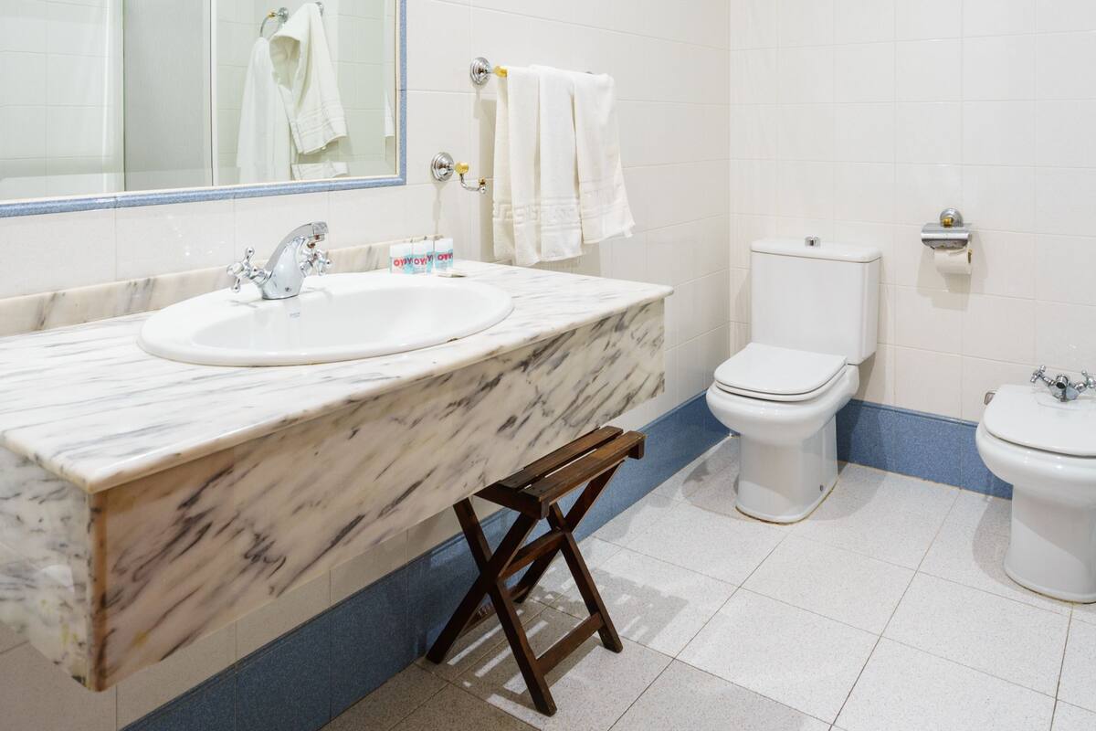 A bathroom with a marble sink, a large mirror, a toilet, and a bidet.