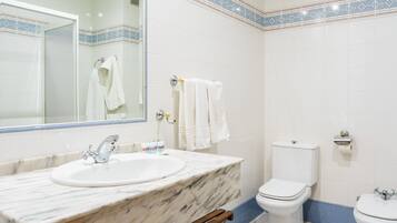 Un baño con lavamanos de mármol, un espejo grande, un inodoro y un bidé.