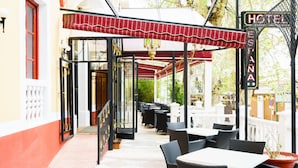 Un área de café al aire libre con mesas y sillas, un espacio de estar cubierto y un letrero que indica un hotel.