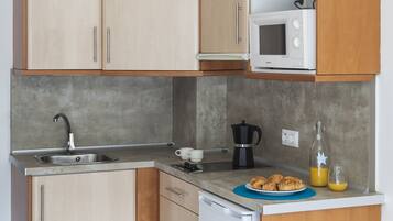 Una cocina compacta con armarios de madera, microondas, lavaplatos, cafetera y pileta.