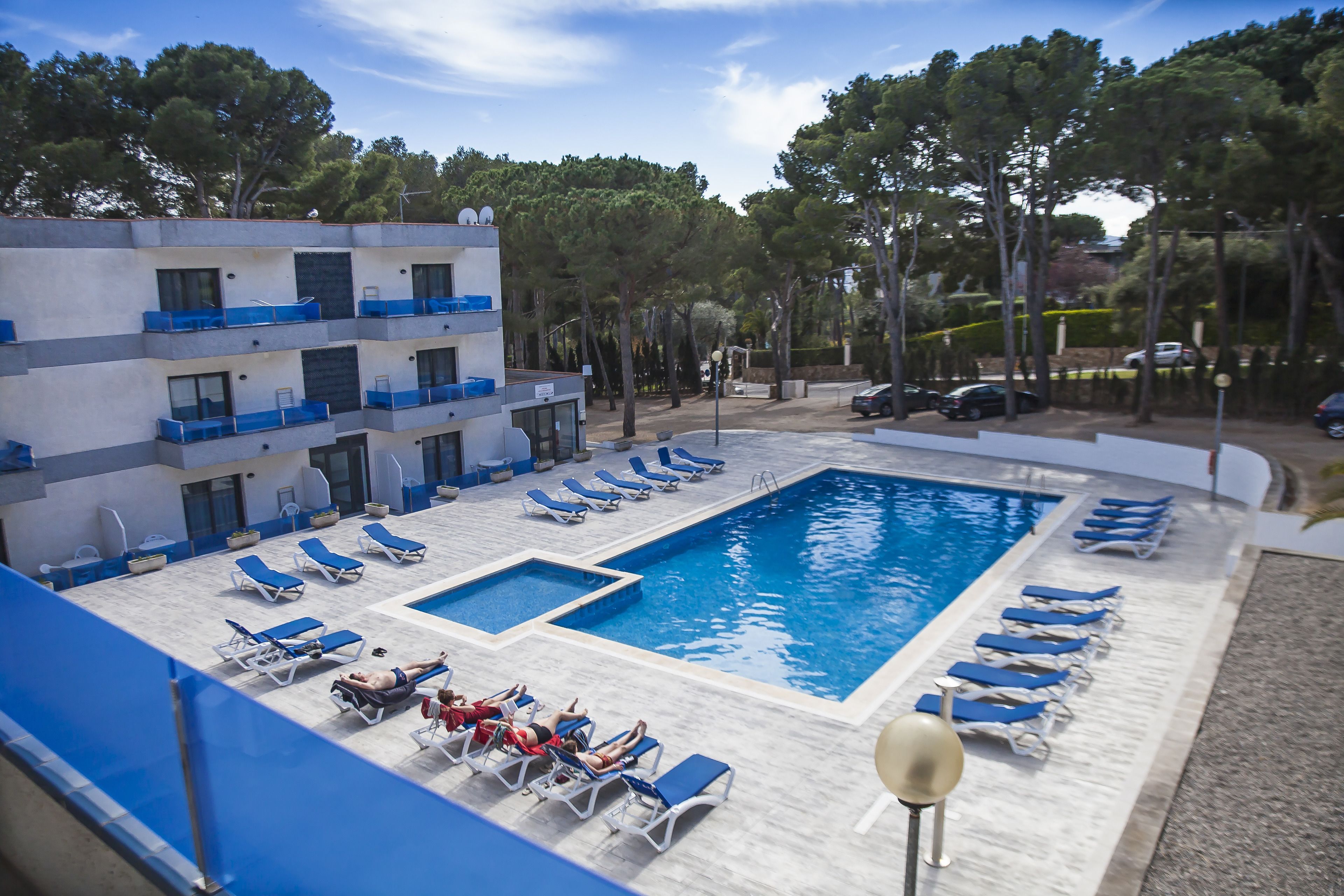 Una piscina con tumbonas y un edificio con balcones.