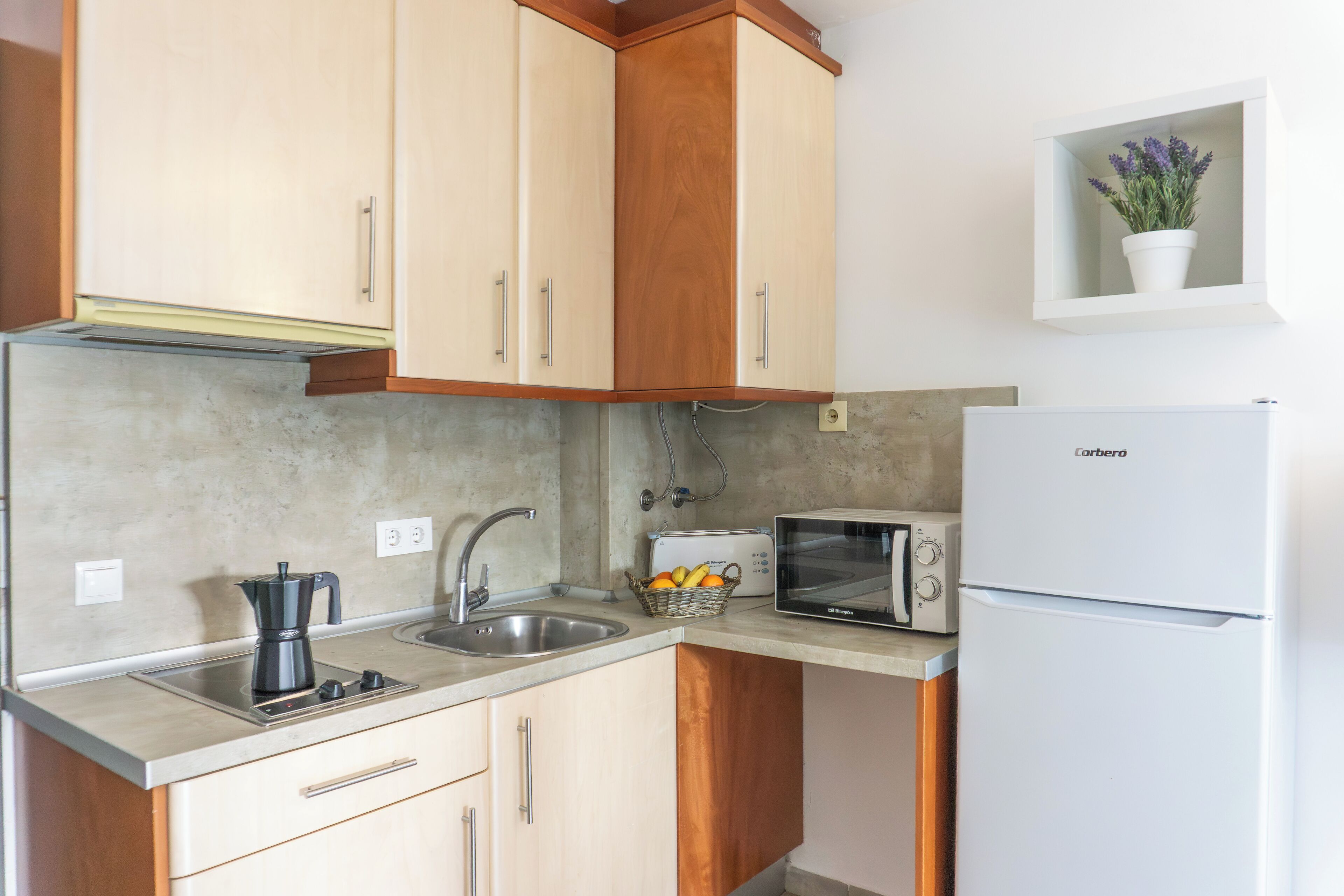 Una cocina compacta con armarios de madera, microondas integrado, cafetera y una pequeña cesta de frutas.