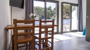 A room with a wooden dining table and chairs, a flat-screen TV mounted on the wall, and a sliding glass door leading to an outdoor area. - RVApartaments Treumal Park (Castell-Platja d'Aro)