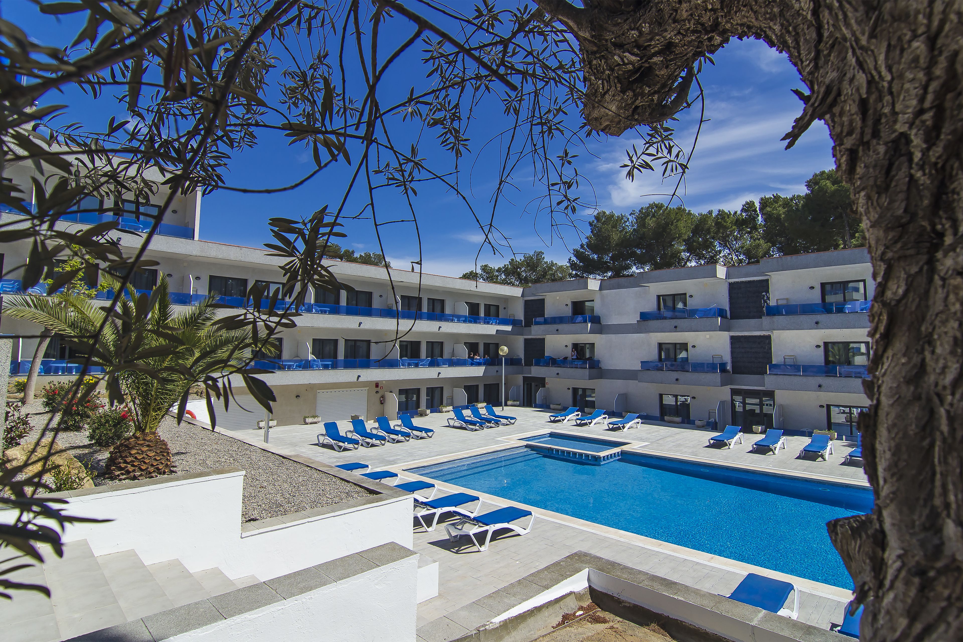 Ein Hotel mit Schwimmbad, mehreren Balkonen und blauem Himmel.