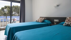 A hotel room with two beds, a balcony, and a table with a chair. - RVApartaments Treumal Park (Castell-Platja d'Aro)