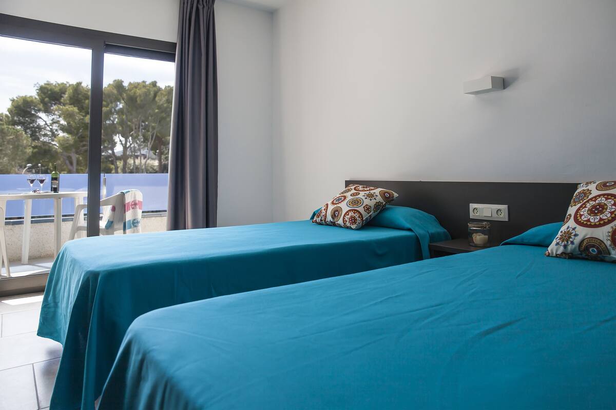 A hotel room with two beds, a balcony, and a table with a chair.