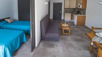 A room with two beds, a sofa, a small table with a cup, and a kitchenette.