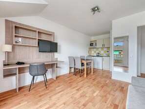 Una sala de estar moderna con un televisor de pantalla plana, un escritorio y una zona de comedor con sillas.