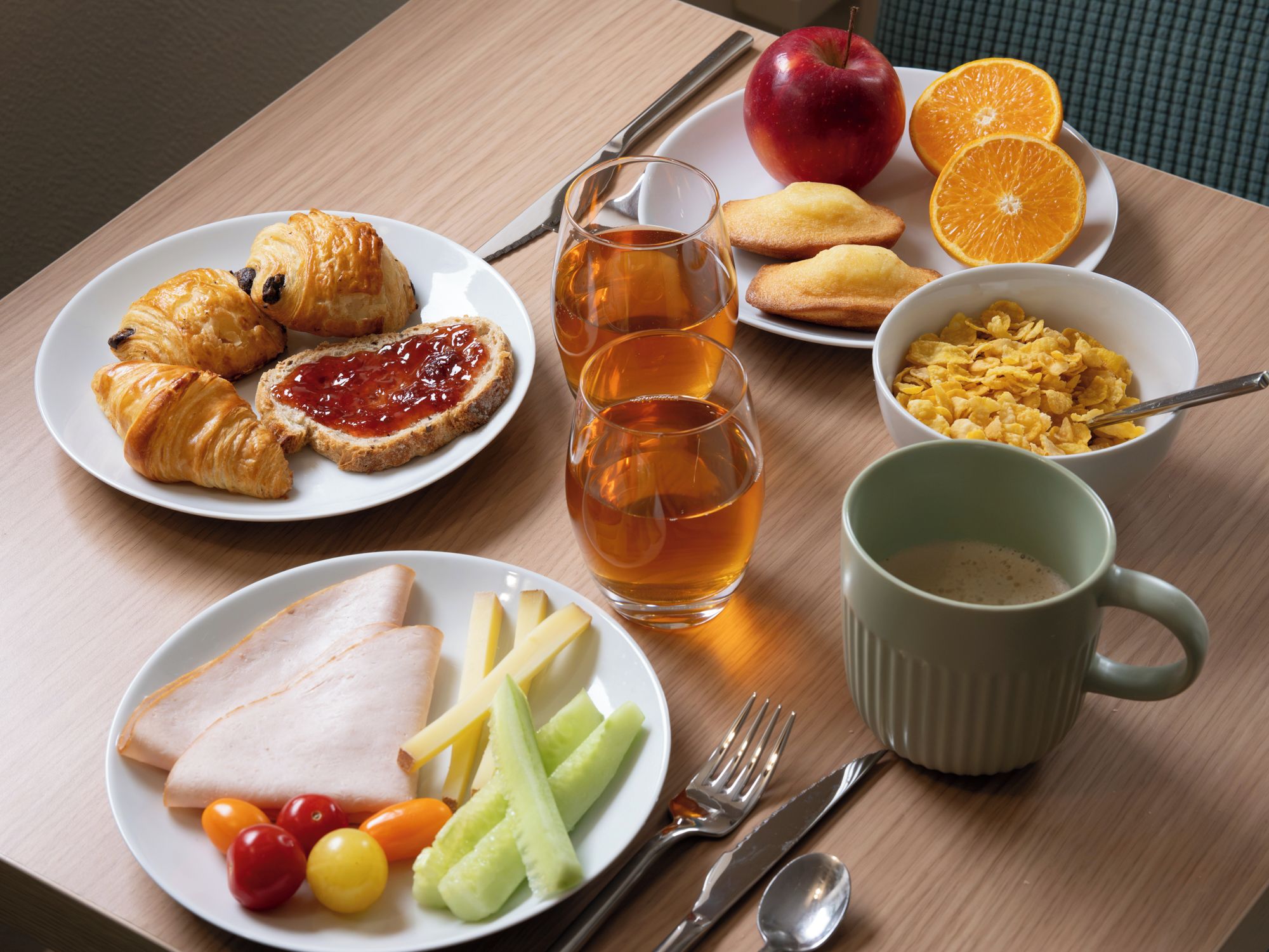 A breakfast table with croissants, jam, fruit, cereal, and a mug.